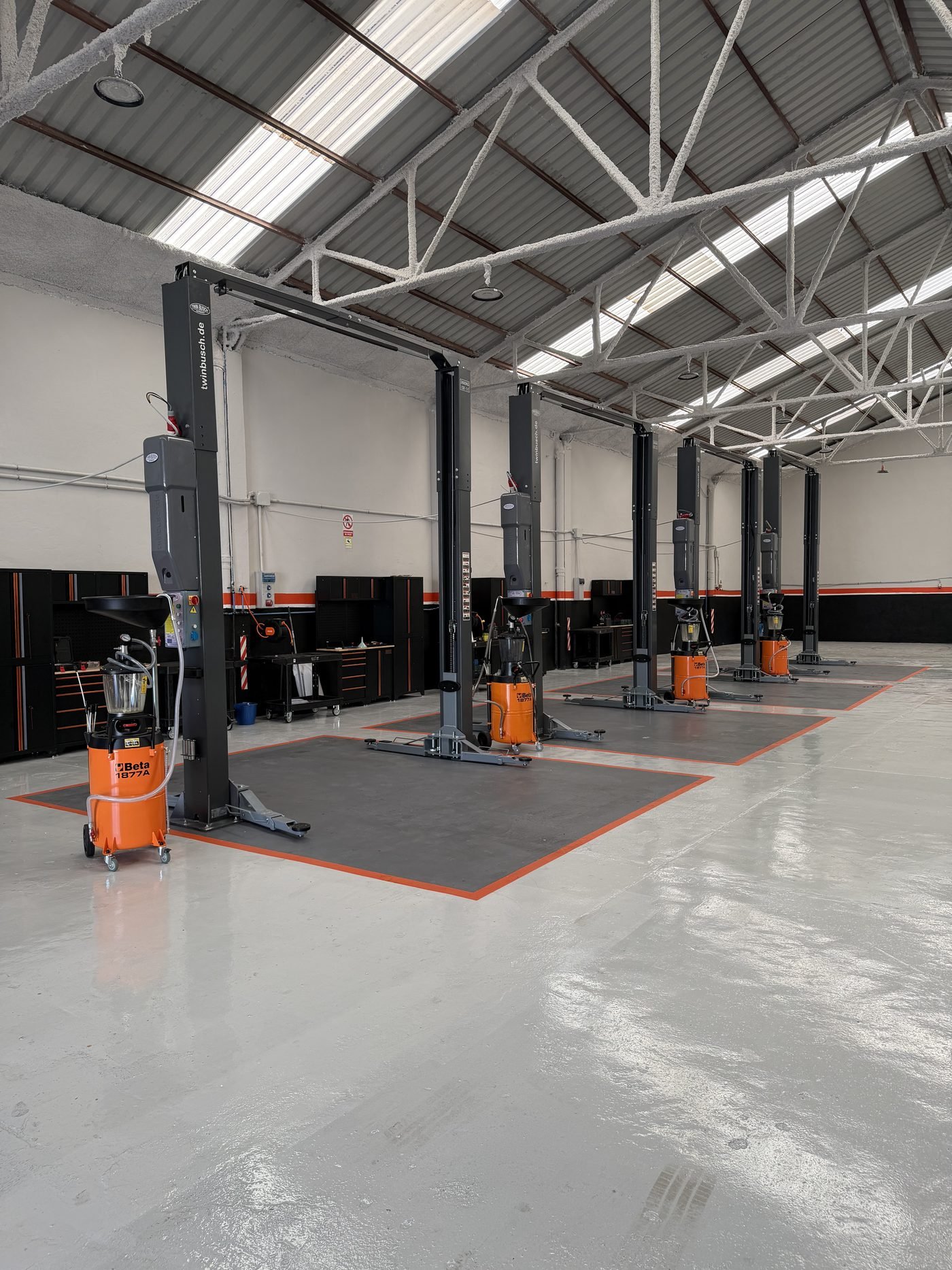 Interior del taller Fast Cambio en Málaga: cuatro elevadores de dos columnas, recuperadores de aceite Beta y suelo epoxi, listos para el cambio de aceite y fluidos.